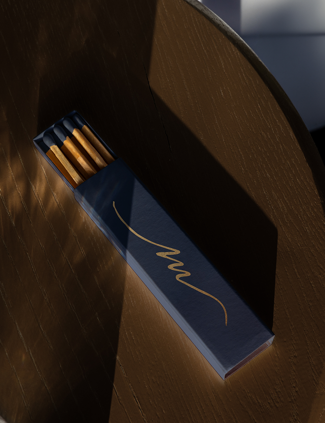 Navy matchbox with gold Maison monogram on a walnut table
